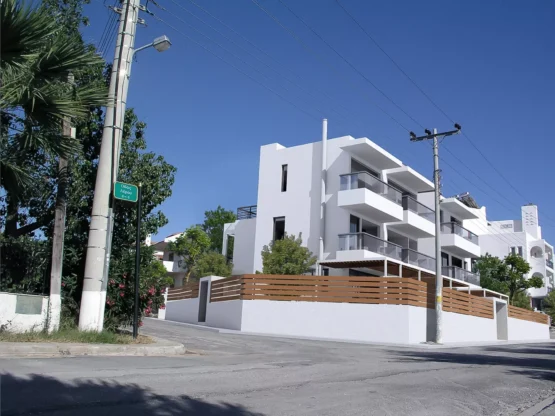 Exterior view of a minimalist residential building at the corner of Lerou and Lypson streets in Panorama Voula (Dikastika), featuring white geometric volumes and glass balconies, designed by ISV Architects and built by Skotidas.
