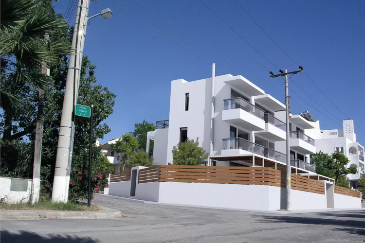 Exterior view of a minimalist residential building at the corner of Lerou and Lypson streets in Panorama Voula (Dikastika), featuring white geometric volumes and glass balconies, designed by ISV Architects and built by Skotidas.