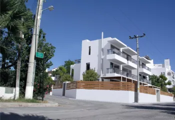 Exterior view of a minimalist residential building at the corner of Lerou and Lypson streets in Panorama Voula (Dikastika), featuring white geometric volumes and glass balconies, designed by ISV Architects and built by Skotidas.