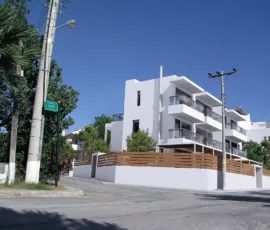Architectural purity and minimalist elegance at the junction of Lerou and Lypson, Panorama Voula. Exterior view of a minimalist residential building at the corner of Lerou and Lypson streets in Panorama Voula (Dikastika), featuring white geometric volumes and glass balconies, designed by ISV Architects and built by Skotidas.