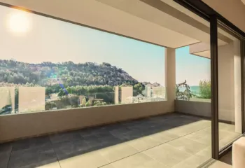 Luxury residential balcony in Galatsi with glass railings, showcasing golden hour sunlight and panoramic views of Veikou Hill.