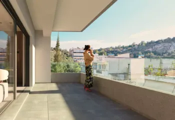 Woman standing on a luxury apartment balcony in Galatsi, overlooking the urban landscape and Veikou Hill during golden hour.