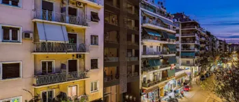 Urban elegance at dusk – The Acharnon 60 residential complex. Atmospheric urban perspective of the Acharnon 60 residential building in Athens at sunset, showing the illuminated facade and city street life.