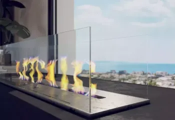 Sustainable warmth with a Mediterranean view. Project: Ikarou 7 | Developer: Thekla Constructions. Macro architectural visualization of a modern glass-protected ethanol fireplace with dancing flames and a blurred coastal city view in Alimos by Thekla Constructions