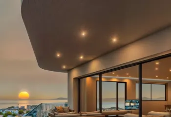 The art of the Athenian sunset. Project: Ikarou 7 | Developer: Thekla Constructions. Luxury penthouse terrace in Alimos at sunset featuring architectural ceiling lights warm interior glow and a panoramic view of the sun setting over the Saronic Gulf by Thekla Constructions