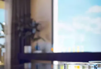 Artistic details of a life well-lived. Project: Ikarou 7 | Developer: Thekla Constructions. Close up lifestyle shot of a coffee cup and water glass on a marble table with a blurred luxury penthouse interior and blue sky background in Alimos by Thekla Constructions