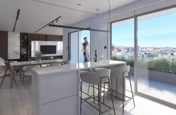 A breathtaking view of the Palaio Faliro Loft interior, showcasing the seamless integration of the kitchen, dining, and living areas with the expansive outdoor terrace. Luxury open-plan apartment interior with marble kitchen island and panoramic balcony view in Palaio Faliro